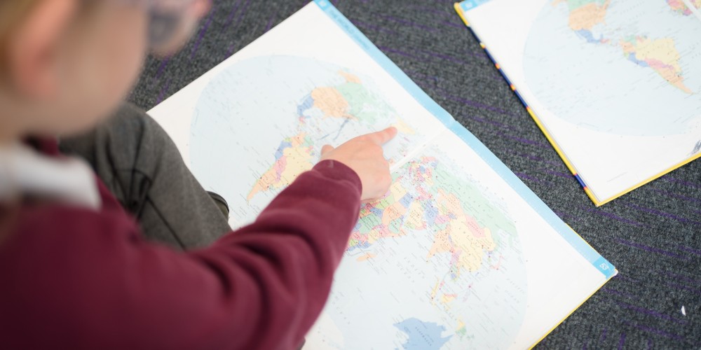 A student points at Greenland on a world map.
